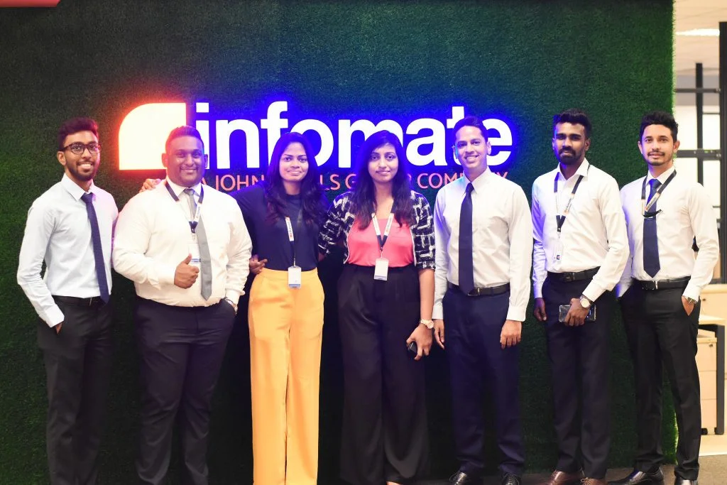 Infomate corporate team members standing together in front of the office brand wall at Infomate,a leading BPO company in Sri Lanka.