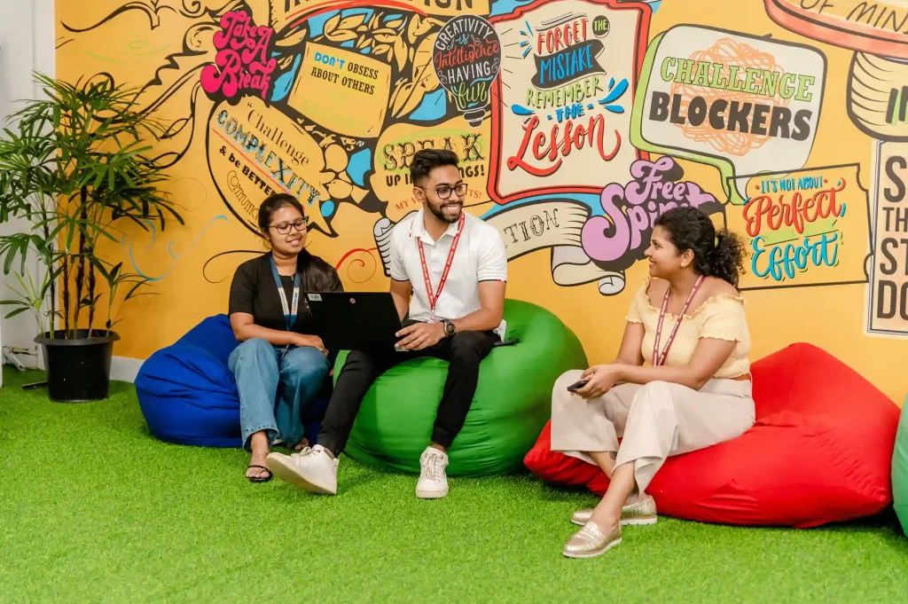 Young corporate professionals collaborating on a laptop in a vibrant, modern breakout area at a leading BPO company in Sri Lanka.